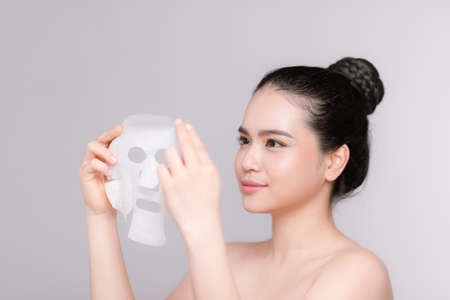 Beauty Skin Care Concept - Beautiful Caucasian Woman applying paper sheet mask on her face white background.の写真素材
