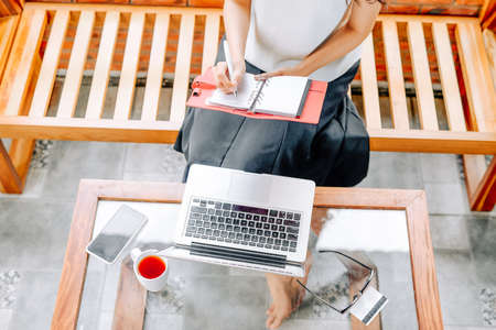 Young asian woman managing her work schedule in her personal diary, taking notes while working on laptop computerの写真素材