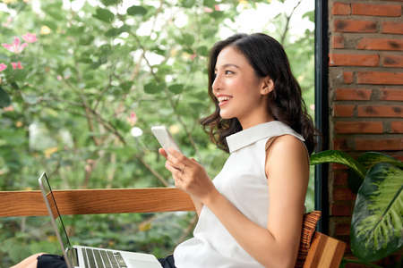 Happy casual beautiful woman is talking on a phone sitting on a sofa at home.の写真素材