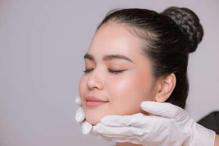 Portrait of a young asian woman getting a beauty medical treatment isolated over gray backgroundの写真素材