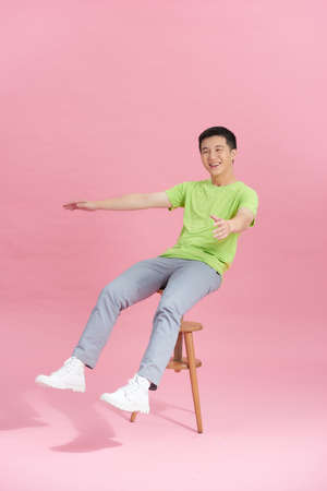 A young man in a greenT-shirt is sitting on a high chair.の写真素材