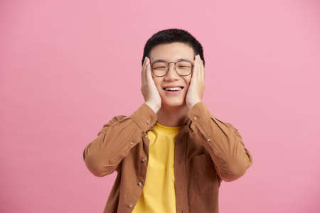 Happy and amazed asian young man touching his face, shocked with unexpected promotion at workの写真素材