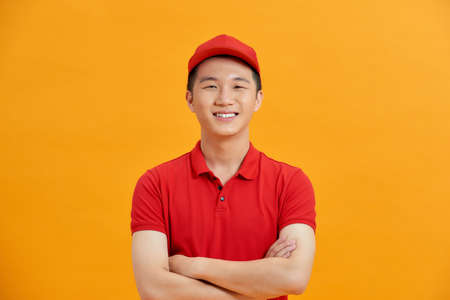 Smiling delivery man in red uniform standing with arm crossed - isolated on white backgroundの写真素材