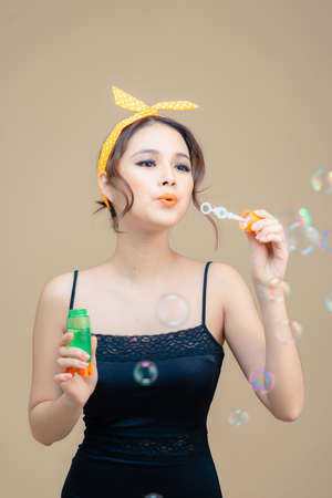 young beautiful female blowing soap bubbles against beige background.の写真素材