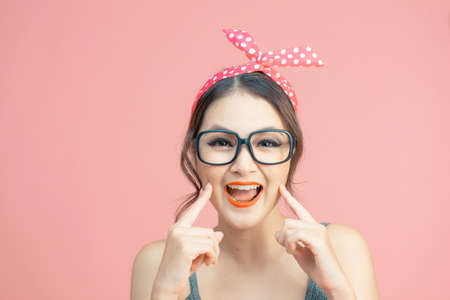 Image of happy asian woman smiling and pointing finger at her cheeks isolated over pink backgroundの写真素材
