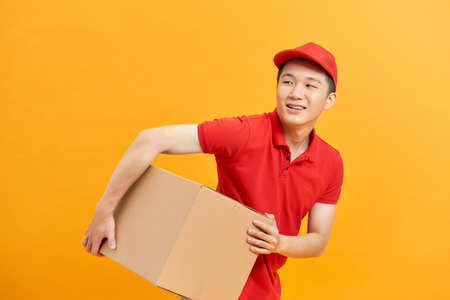 Cheerful delivery man. Happy young courier holding a cardboard box and smiling while standing against white backgroundの写真素材