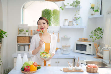 Close up portrait of cute girl eating salad on kitchenの写真素材