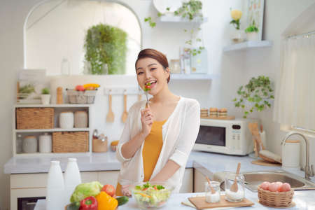 Beautiful Smiling Woman Eating Fresh Organic Vegetarian Salad In Modern Kitchenの写真素材