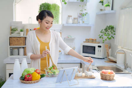 Woman in kitchen preparing vegetables and using tabletの写真素材