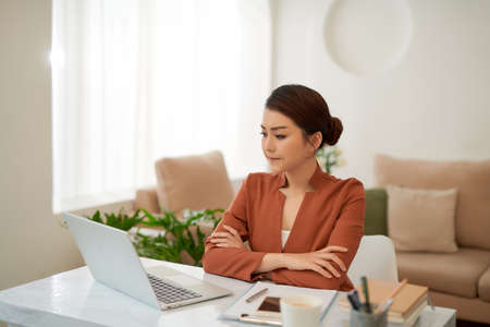 Mature successful business woman looking at mobile cell phone while at home in office work spaceの写真素材