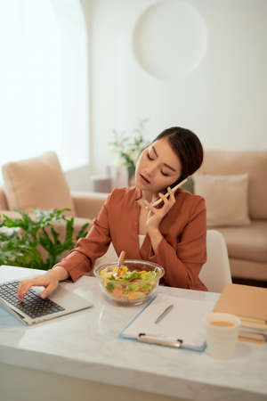 Pretty woman smiling while working from home, on the phone with a saladの写真素材