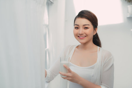 Morning portrait of young smiling woman drinking milkの写真素材