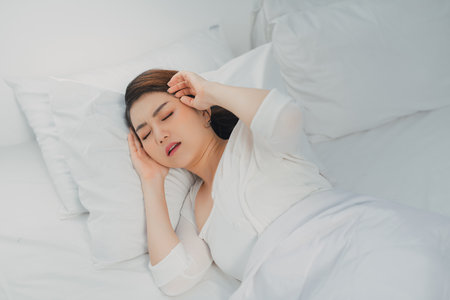 Beautiful young woman suffering from headache while lying in bedの写真素材