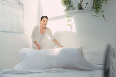 young beautiful woman making her bed early in the morning looking happyの写真素材