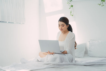 Young woman using laptop computer on a cold winter day in the bedroom.の写真素材