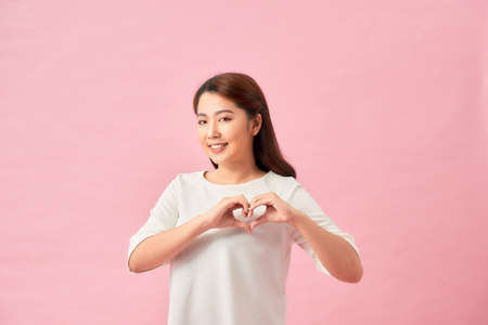 Closeup portrait smiling cheerful happy young woman making heart sign with hands isolated pink backgroundの写真素材