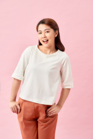 Young working woman smiling and looking at camera, standing on pink background.の写真素材