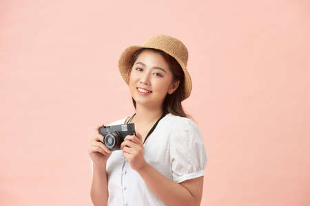 pretty cool young woman model with retro film camera wearing a elegant hat over pink backgroundの写真素材