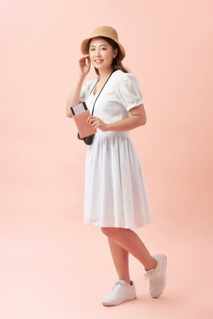 Full length of a happy young woman standing isolated over pink background, holding photo camera, showing passport with flight ticketsの写真素材