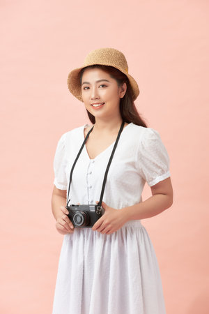 Portrait of a smiling young woman in summer hat standing with photo camera isolated over pink backgroundの写真素材