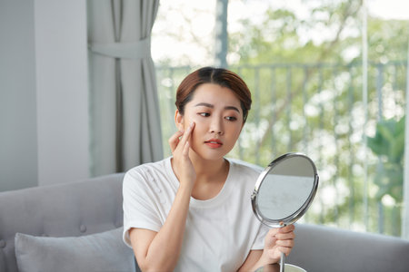 beautiful young woman examining her face in the mirrorの写真素材
