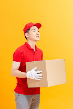 Handsome young delivery man with box isolated on yellow background.の写真素材