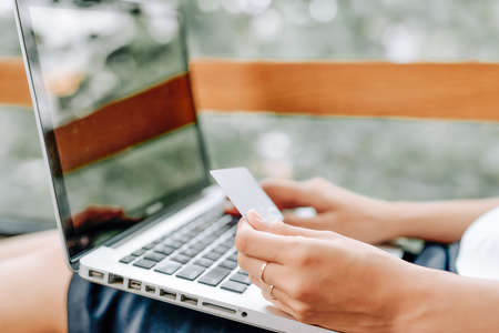 Beautiful young woman working on laptop computer while sitting at the living room, showing credit cardの写真素材