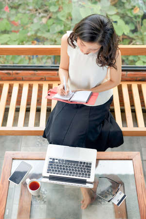 Young pretty woman sitting on the sofa, working with diary and notebookの写真素材