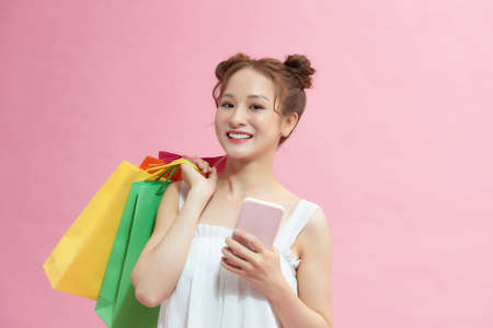 happy woman using smartphone and holding shopping bags isolated on pinkの写真素材
