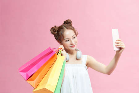 Asian beautiful happy young woman holding smartphone for selfie and shopping online with shopping bags on pink background.の写真素材