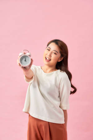 Young Asian woman with a clock on pink backgroundの写真素材