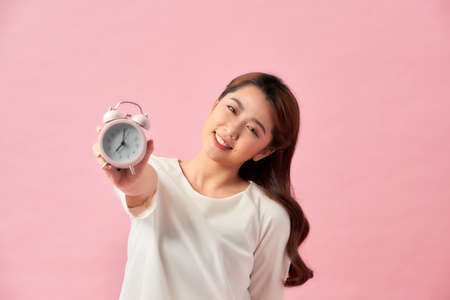 Young Asian woman with a clock on pink backgroundの写真素材