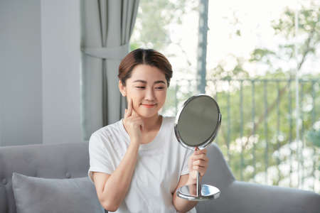 beautiful young woman examining her face in the mirrorの写真素材