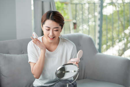 Pretty asian woman applying powder foundation on her faceの写真素材