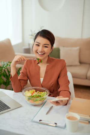 woman with laptop in modern office interior, eating lunch.の写真素材