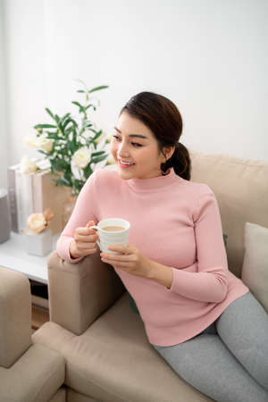 Pretty young lady relaxing with tea cup at living room.の写真素材