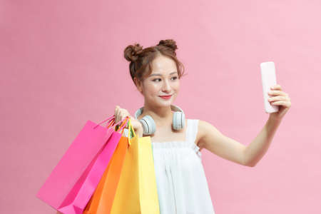 Happy young woman with shopping bags taking selfie on pink backgroundの写真素材