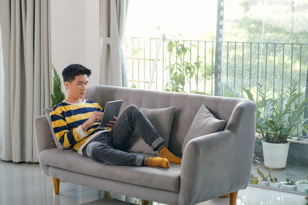Man using digital tablet on sofa at home.の写真素材