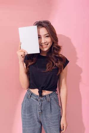 Portrait young happy asian woman book covering your eye smiling positive emotion on pink backgroundの写真素材
