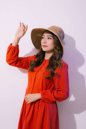 Portrait of a smiling attractive woman in summer dress and hat posing while standing and looking at camera isolated over pink backgroundの写真素材