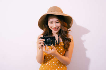 Close up portrait of a smiling pretty girl in dress taking photo on a retro camera isolated over pink backgroundの写真素材