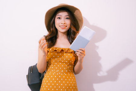 Cheerful young woman standing isolated over pink background, showing passport with flight ticketsの写真素材