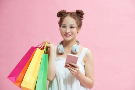 happy woman using smartphone and holding shopping bags isolated on pinkの写真素材