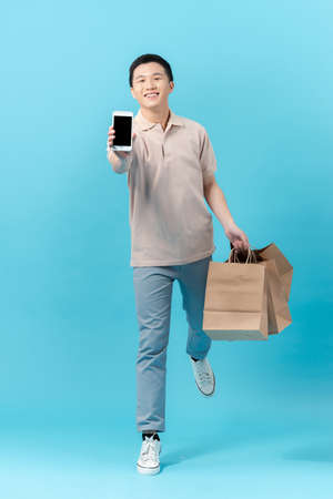 Asian man holding smartphone and shopping bag while jumpingの写真素材