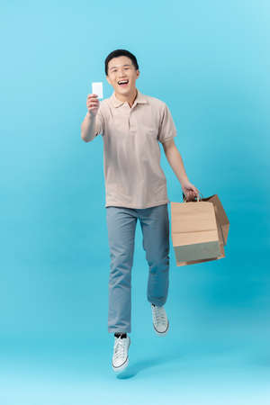 happy smiling handsome Asian man carrying shopping bags and showing credit card in light blueの写真素材