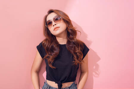 Beautiful cheerful confident young woman standing with arms behind head over a pink backgroundの写真素材