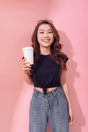 Photo of pensive woman holding takeout coffee stands over pink wallの写真素材
