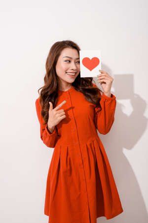 surprised asian young woman holding greeting card while standing isolated on pinkの写真素材
