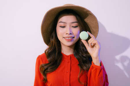 Portrait of a beautiful young woman wearing red dress standing isolated over white background, holding macaroonsの写真素材
