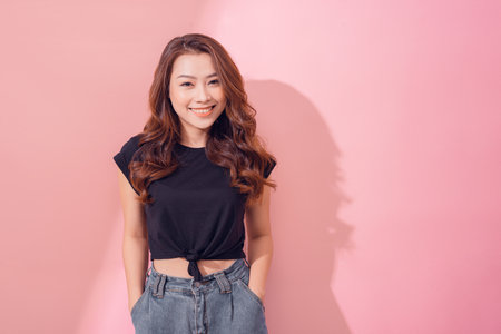Portrait of charming curly-haired woman in trendy garment smiling broadly and glancing at camera over pastel background.の写真素材
